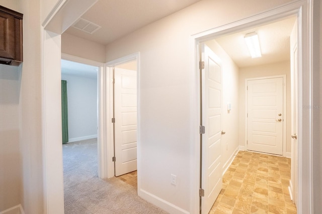 hallway featuring visible vents, light carpet, and baseboards