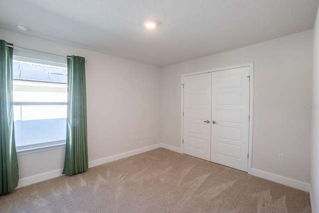 unfurnished bedroom featuring carpet floors, a closet, a textured ceiling, and baseboards