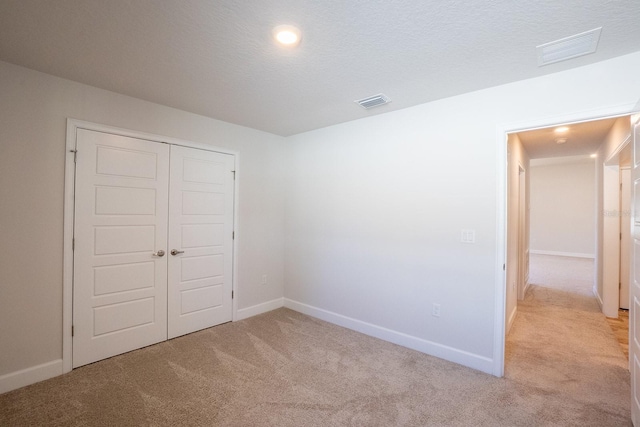 unfurnished bedroom with light carpet, a textured ceiling, visible vents, and baseboards