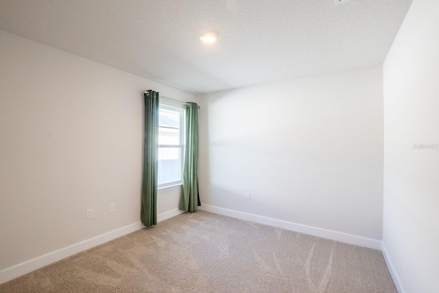 spare room featuring light colored carpet and baseboards