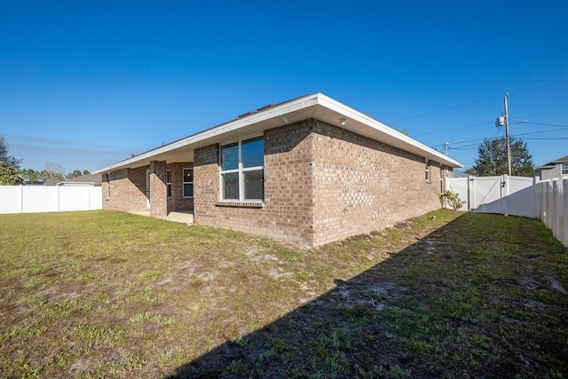 rear view of property with a gate, brick siding, a yard, and a fenced backyard