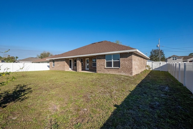 rear view of house with a shingled roof, brick siding, a yard, and a fenced backyard