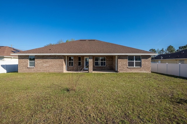 back of house featuring a shingled roof, fence private yard, brick siding, and a lawn