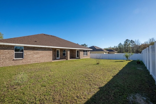 back of house featuring a yard, brick siding, a shingled roof, and a fenced backyard