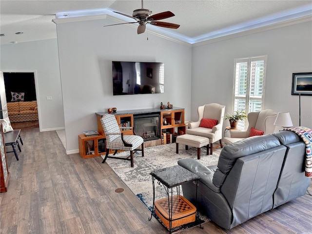 living area with a ceiling fan, wood finished floors, a glass covered fireplace, baseboards, and vaulted ceiling