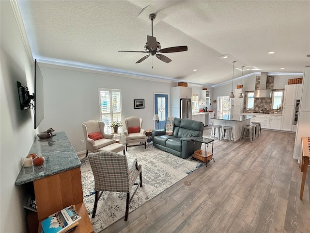 living room with light wood-type flooring, lofted ceiling, a textured ceiling, and ornamental molding