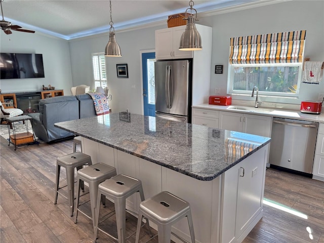 kitchen with wood finished floors, a sink, appliances with stainless steel finishes, a kitchen breakfast bar, and a center island