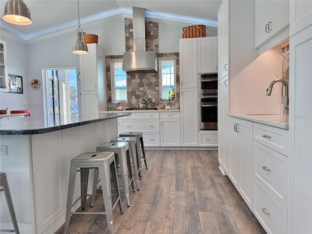 kitchen featuring a sink, appliances with stainless steel finishes, white cabinetry, wall chimney range hood, and tasteful backsplash