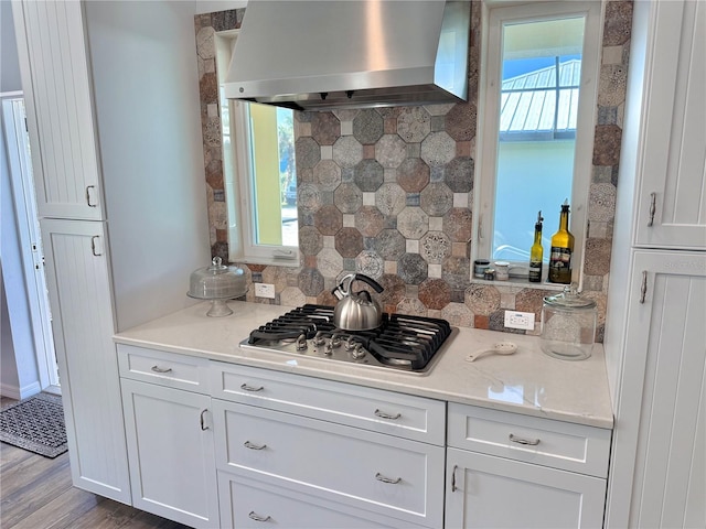 kitchen with wood finished floors, stainless steel gas cooktop, white cabinets, wall chimney exhaust hood, and tasteful backsplash