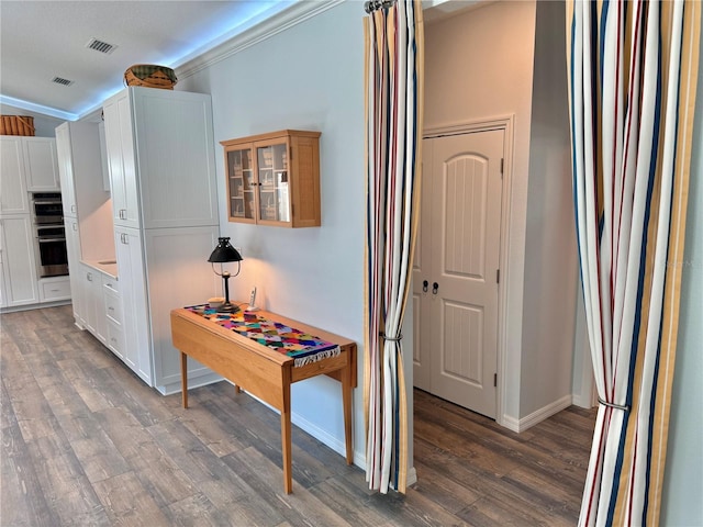 hallway with visible vents, ornamental molding, baseboards, and wood finished floors