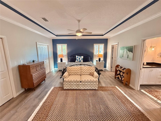 bedroom featuring a tray ceiling, crown molding, light wood-style floors, and visible vents