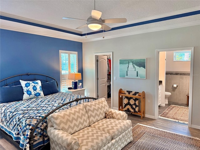 bedroom with a textured ceiling, wood finished floors, a closet, crown molding, and a spacious closet