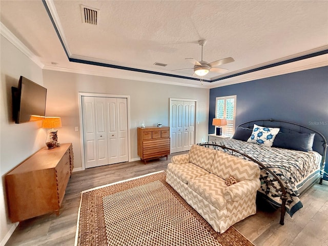 bedroom with visible vents, crown molding, multiple closets, a tray ceiling, and wood finished floors