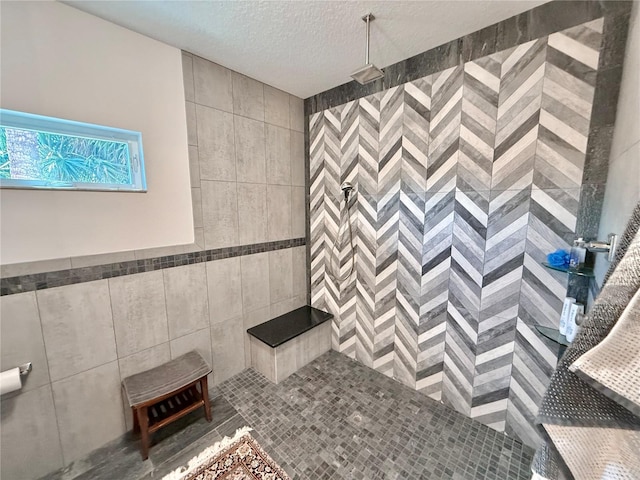 bathroom featuring a tile shower, a textured ceiling, and tile walls