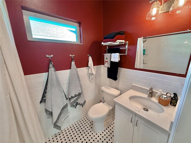 full bath with toilet, a shower with shower curtain, tile walls, wainscoting, and vanity