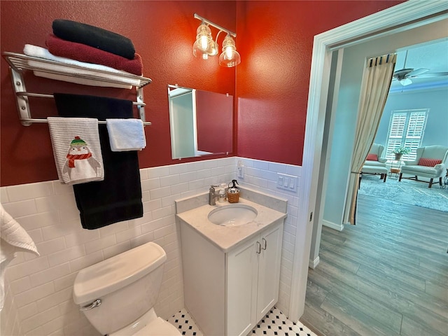 bathroom with toilet, wood finished floors, tile walls, wainscoting, and vanity