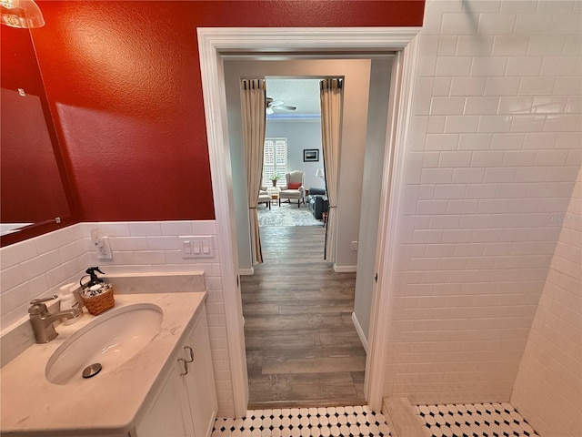 bathroom featuring wood finished floors, a tile shower, tile walls, crown molding, and vanity