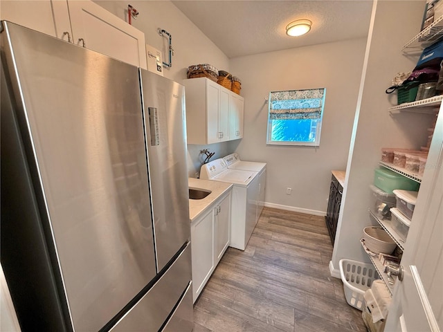 washroom featuring washing machine and clothes dryer, baseboards, light wood-type flooring, cabinet space, and a textured ceiling