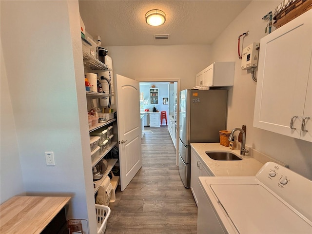 laundry area with dark wood-style flooring, separate washer and dryer, cabinet space, a textured ceiling, and a sink