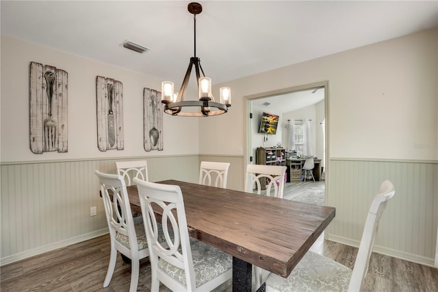 dining area with wood finished floors, a wainscoted wall, visible vents, and an inviting chandelier