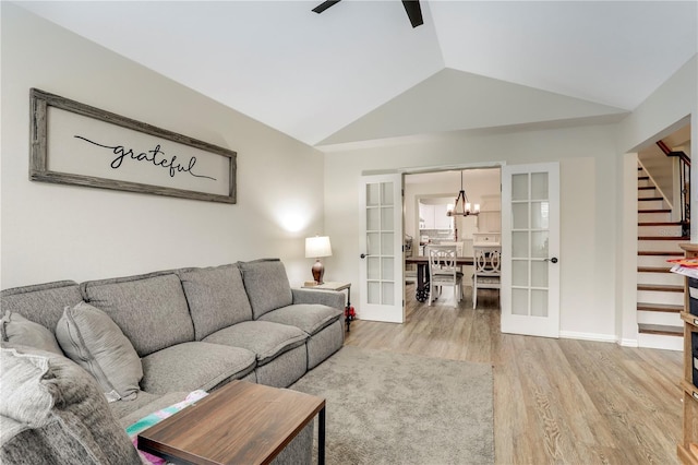 living area featuring lofted ceiling, ceiling fan with notable chandelier, wood finished floors, stairs, and french doors