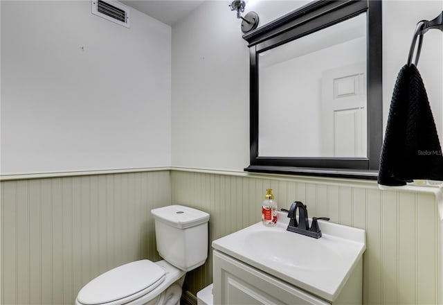 half bath featuring visible vents, toilet, wainscoting, and vanity