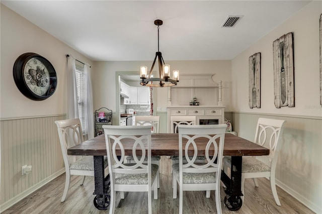 dining room with light wood-type flooring, a wainscoted wall, visible vents, and a notable chandelier