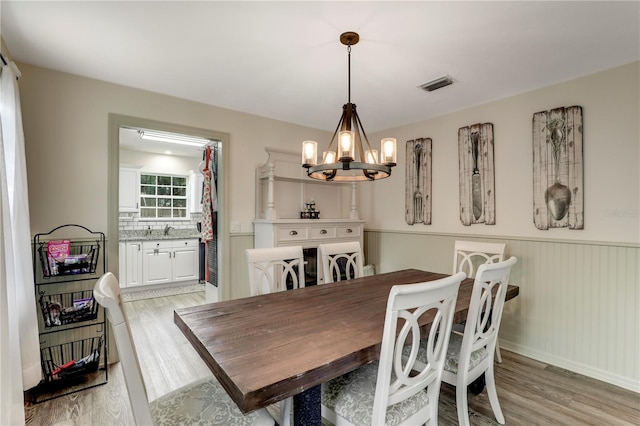 dining space featuring light wood-style floors, a notable chandelier, visible vents, and a wainscoted wall