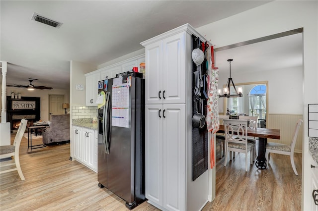 kitchen with decorative light fixtures, visible vents, wainscoting, white cabinets, and stainless steel fridge with ice dispenser