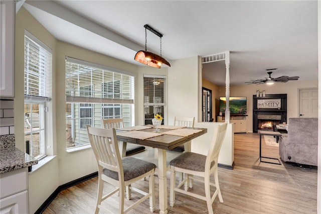 dining area featuring visible vents, a lit fireplace, light wood-type flooring, and a ceiling fan