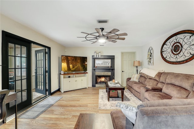 living area featuring visible vents, ceiling fan, light wood-type flooring, a lit fireplace, and baseboards