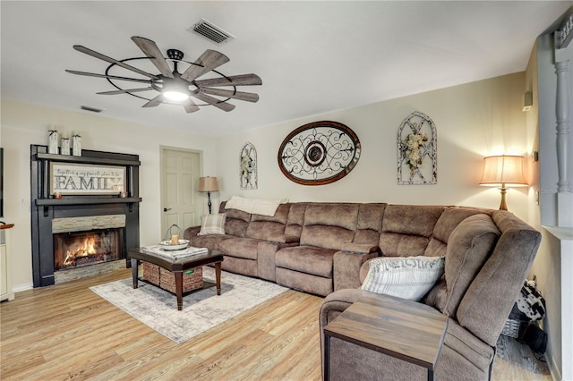 living area with visible vents, ceiling fan, a lit fireplace, and wood finished floors