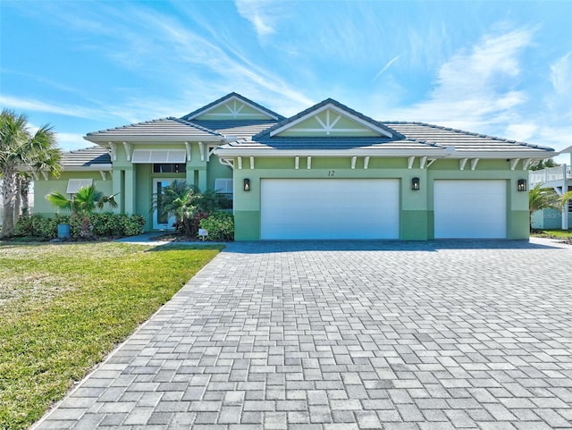 view of front of home with decorative driveway, an attached garage, a tile roof, and stucco siding