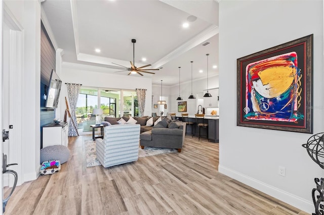 living room with a tray ceiling, crown molding, recessed lighting, light wood-type flooring, and baseboards