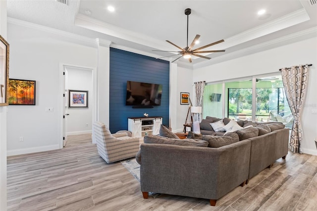 living area with ornamental molding, a tray ceiling, light wood-type flooring, and a ceiling fan