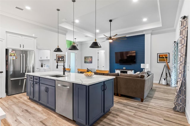 kitchen with a raised ceiling, appliances with stainless steel finishes, ornamental molding, white cabinetry, and a sink