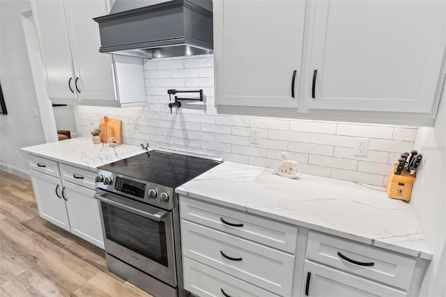 kitchen featuring stainless steel electric range oven, custom exhaust hood, and white cabinetry