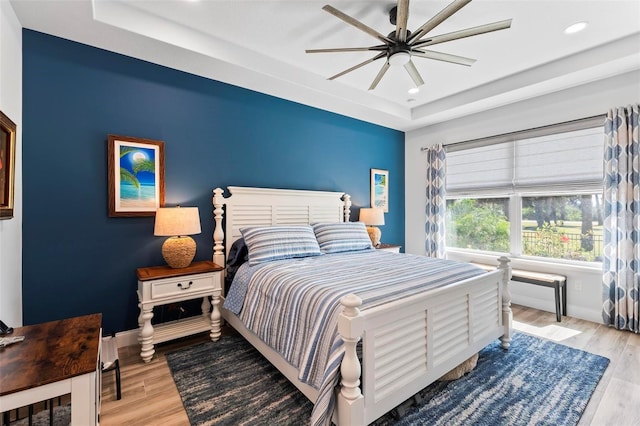 bedroom with baseboards, recessed lighting, a raised ceiling, and light wood-style floors