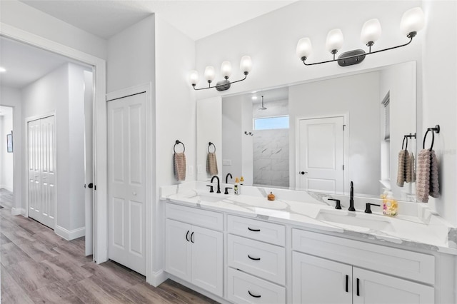 full bath with double vanity, a sink, a tile shower, and wood finished floors