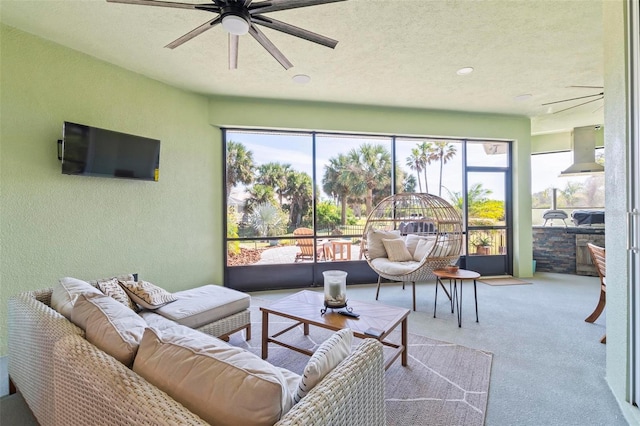 living area with a ceiling fan, a textured wall, a sunroom, carpet flooring, and a textured ceiling