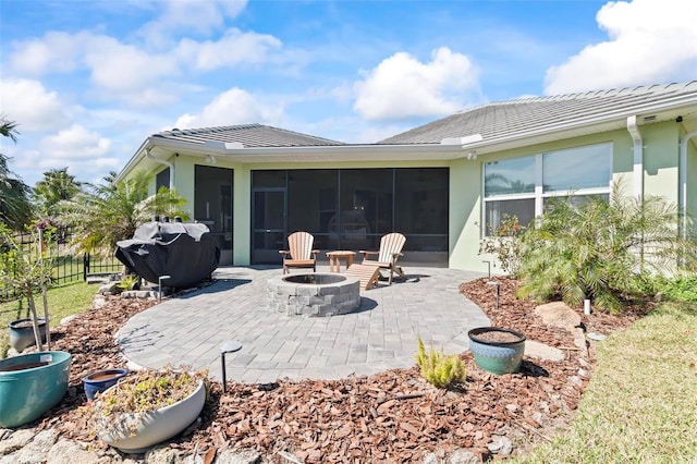 rear view of house with an outdoor fire pit, a patio, a sunroom, fence, and stucco siding