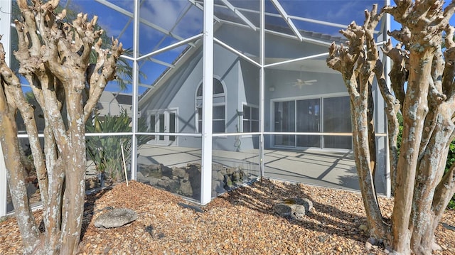 view of side of home with ceiling fan, glass enclosure, and a patio