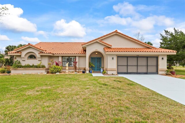 mediterranean / spanish home with an attached garage, driveway, a tiled roof, stucco siding, and a front yard