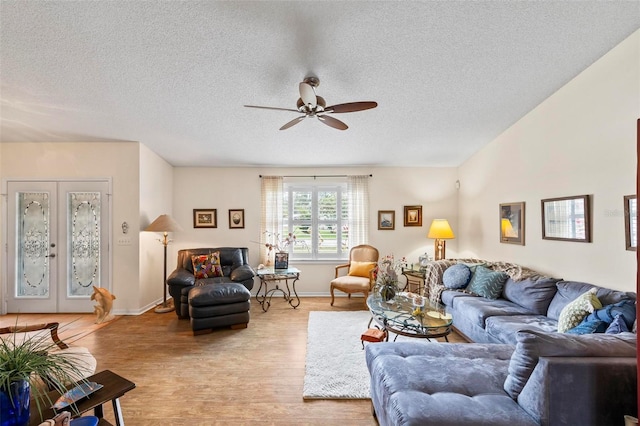 living area featuring a textured ceiling, light wood-type flooring, a ceiling fan, and baseboards