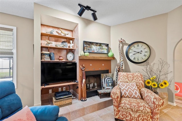 living room with baseboards, arched walkways, a tiled fireplace, a textured ceiling, and light tile patterned flooring