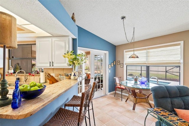 kitchen with a peninsula, vaulted ceiling, light countertops, white cabinetry, and pendant lighting