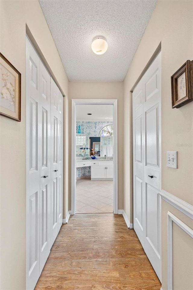 corridor featuring baseboards, light wood-style flooring, and a textured ceiling