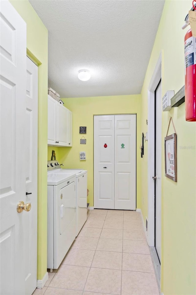 laundry room featuring cabinet space, light tile patterned flooring, a textured ceiling, separate washer and dryer, and baseboards