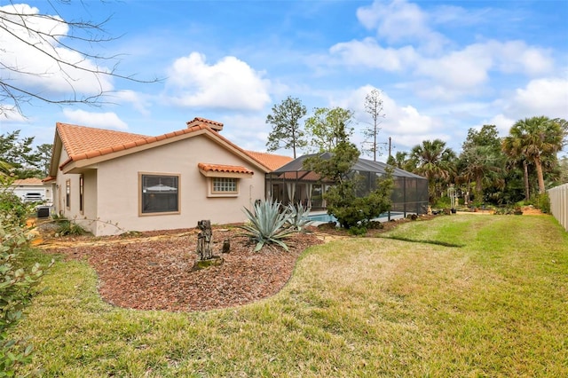 exterior space with a lawn, a tile roof, a lanai, fence, and stucco siding