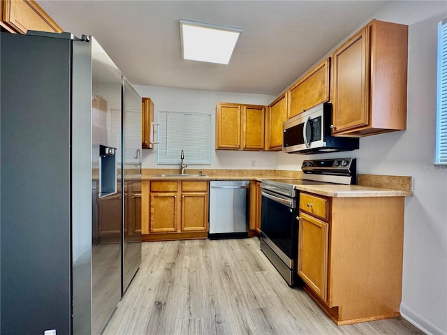 kitchen with light countertops, appliances with stainless steel finishes, a sink, and brown cabinets